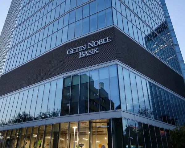 Nowoczesny budynek banku z napisem "GETIN NOBLE BANK". W szklanej fasadzie odbijają się inne budynki i drzewa.