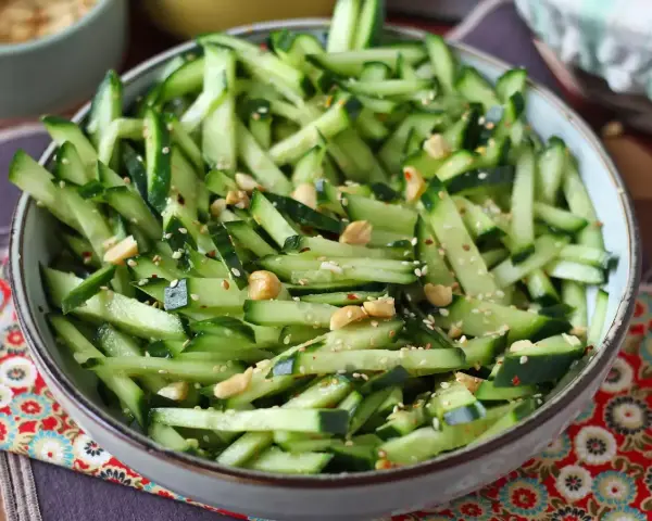 Una ciotola di fresca insalata di cetrioli tagliati a julienne, condita con semi di sesamo e arachidi croccanti.
