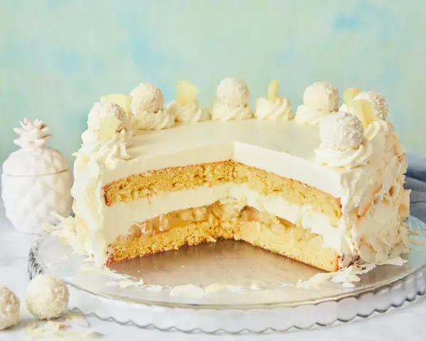 Eine köstliche Piña Colada Torte mit Kokosraspeln und Ananasstücken, verziert mit Sahnetuffs und Pralinen.