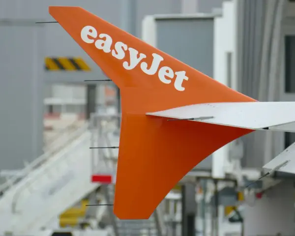 Pomarańczowy statecznik pionowy samolotu easyJet z białym logo, gotowy do przyjęcia bagażu pasażerów.