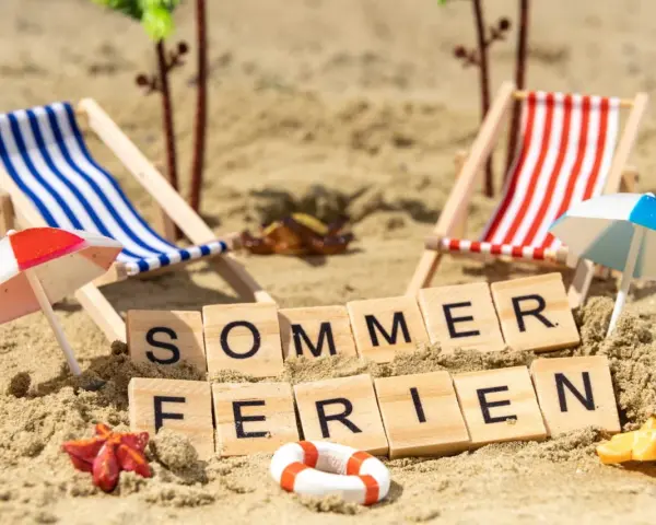 Strandkörbchen, Palmen und die Worte "Sommerferien" im Sand. Perfekt für die Sommerferien in Brandenburg!