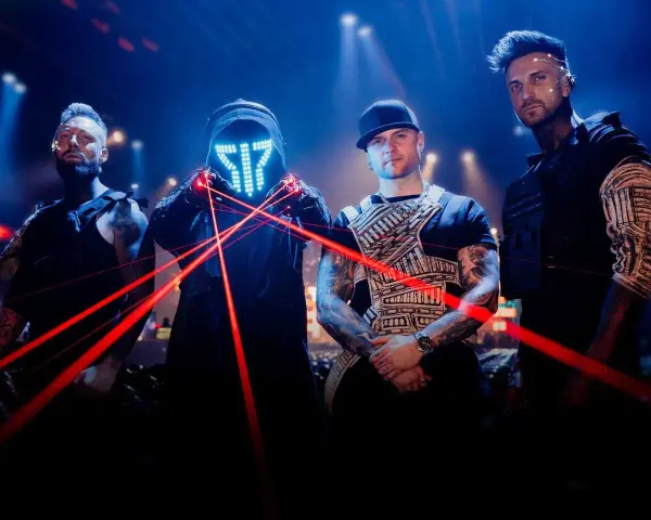 Czterech mężczyzn w futurystycznych strojach, z maską LED i czerwonymi laserami na scenie.