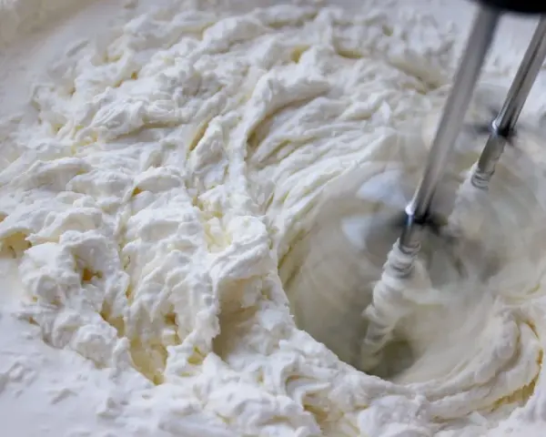 Batidora eléctrica batiendo crema blanca y espesa en un bol.
