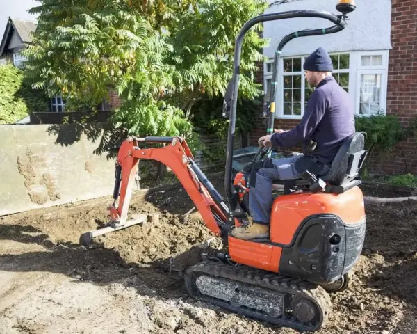 Un ouvrier manœuvre une mini-pelle orange pour des travaux de terrassement. Le prix du terrassement au m2 est une préoccupation pour ce chantier.