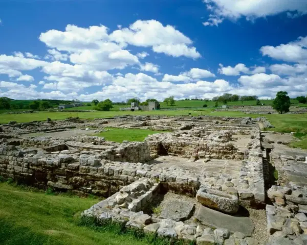 Extensive roman ruin spread across a green field under a blue sky with fluffy clouds.
