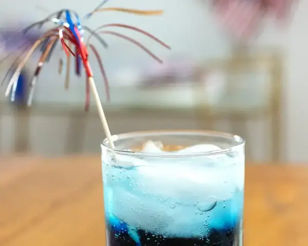 Orzeźwiający drink z grenadyną i blue curacao, ozdobiony kolorową parasolką, idealny na letnie popołudnie.