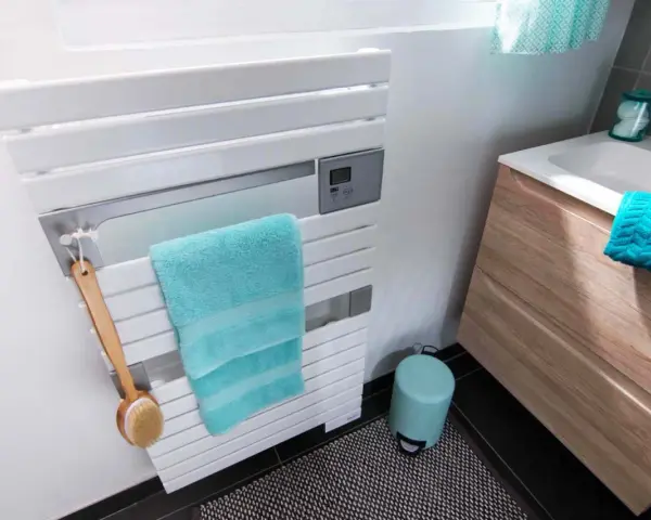 Un sèche-serviettes blanc moderne, avec une serviette turquoise et une brosse de bain en bois. La hauteur du sèche-serviette est idéale pour un accès facile.
