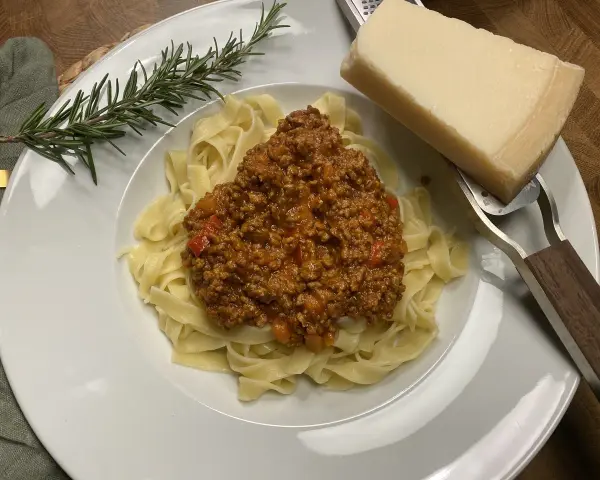 Ein Teller Tagliatelle mit herzhafter Bolognese, garniert mit Rosmarin und Parmesan.