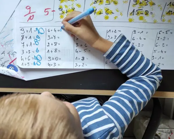 Dziecko rozwiązuje zadania matematyczne. Na kartce widać różne działania, a obok nich cyfry, które mogą stanowić **skalę ocen** lub odpowiedzi.