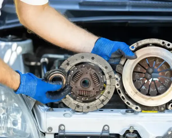 Mechanik w niebieskich rękawiczkach pokazuje zużyte części sprzęgła, które mogą być przyczyną ślizgającego się sprzęgła objawy.