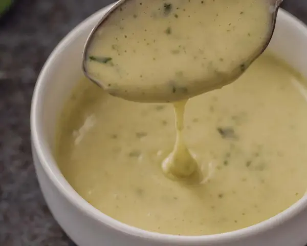 Cremige Sauce Béarnaise tropft von einem Löffel in eine weiße Schüssel.