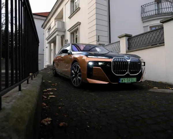 Eleganckie BMW i7 w miedzianym kolorze, zaparkowane przed willą. Ten luksusowy samochód elektryczny oferuje imponujący zasięg, pozwalając na długie podróże.