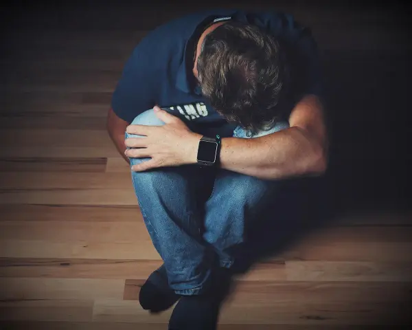 Mężczyzna siedzi skulony na podłodze, opierając głowę na kolanach.