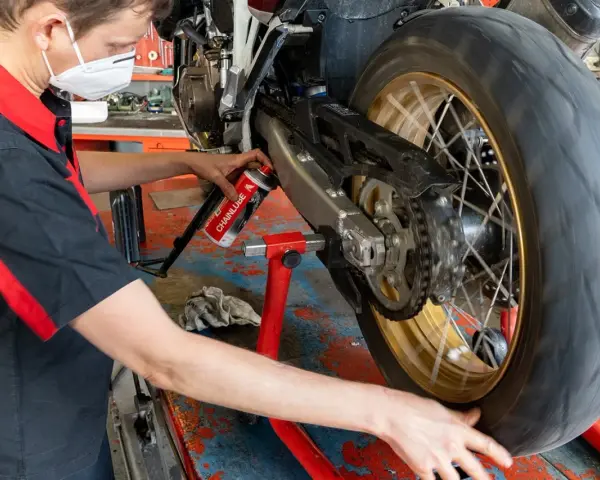 Meccanico lubrifica la catena di una moto. La pulizia catena moto ogni quanti km è fondamentale per la sua durata.
