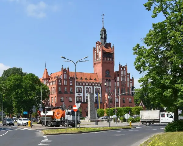 Imponujący ratusz w Słupsku, jedna z głównych atrakcji miasta, góruje nad placem. W tle zielone drzewa i błękitne niebo.