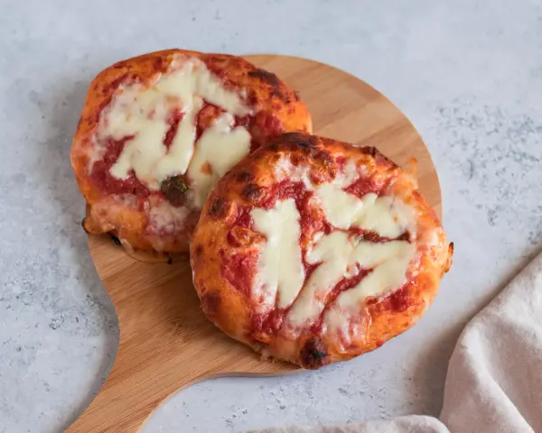 Due pizzette fatte in casa, con pomodoro e mozzarella filante, su un tagliere di legno.