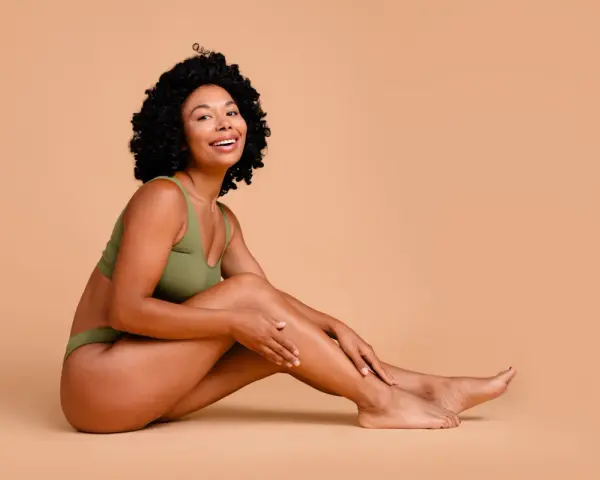 Femme souriante en sous-vêtements verts, caressant sa jambe. Elle partage ses secrets pour comment avoir des pieds doux.