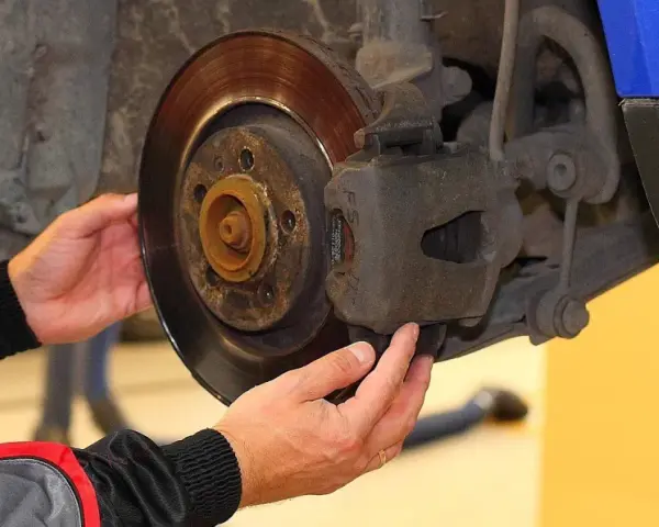 Mechanik sprawdza klocki hamulcowe, dotykając zacisku i tarczy hamulcowej.
