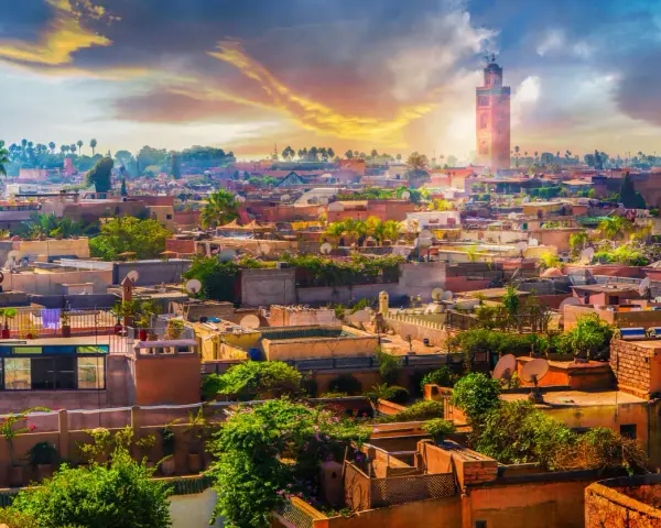 Widok na miasto z minaretem w tle, gdzie leży Marakesz. Dachy domów, palmy i zieleń tworzą malowniczy krajobraz.