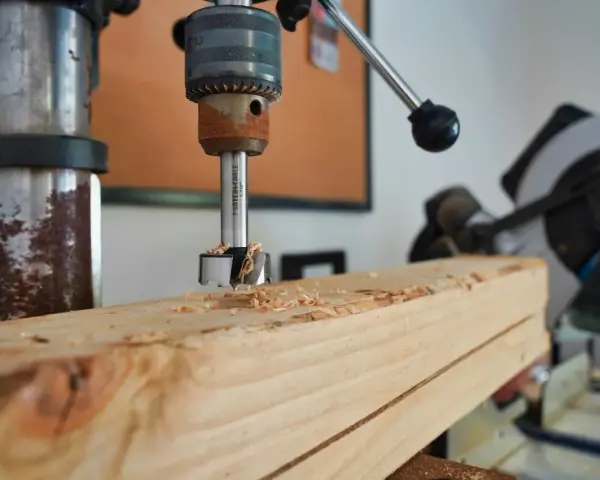 Trapano a colonna che fora un pezzo di legno, creando trucioli. Un esempio pratico di come avvitare una vite nel legno, o meglio, preparare il foro.