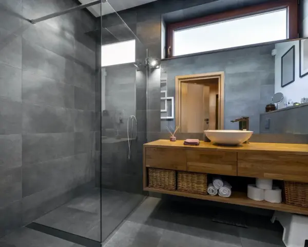 Salle de bain moderne avec douche à l'italienne, carrelage gris, meuble en bois et vasque. Le pose carrelage douche italienne est impeccable.