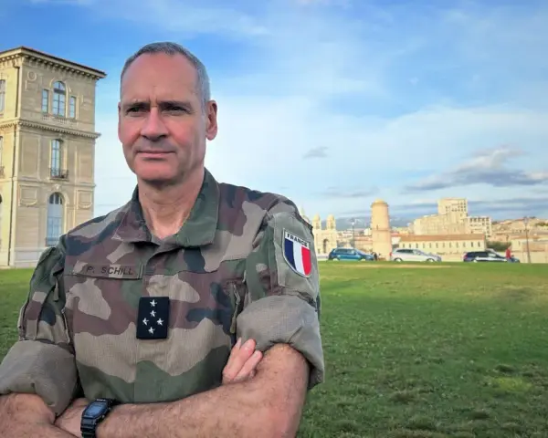 Un officier français, P. Schill, pose devant un bâtiment historique. Comment retrouver un officier ? Il suffit de regarder son uniforme et son insigne.