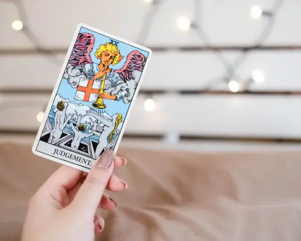 Una mano sostiene la carta de **el juicio tarot**, mostrando un ángel con trompeta y personas resucitando.