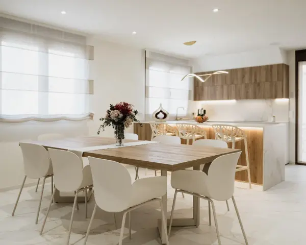 Elegantes cocinas abiertas al salón con barra, mesa de comedor y sillas blancas.