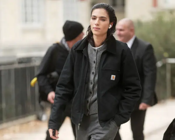 Donna con giacca Carhartt nera e cardigan grigio, cuffiette bianche, cammina con sicurezza.