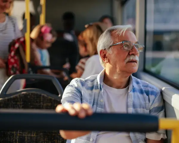 Starszy pan w okularach podróżuje autobusem, ciesząc się darmową komunikacją miejską.