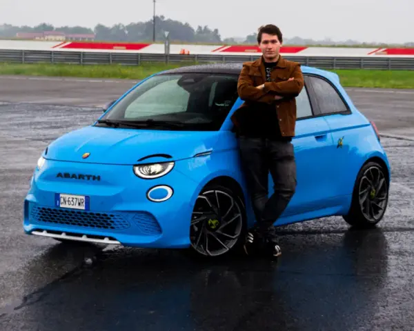 Mężczyzna opiera się o jaskrawo niebieski Abarth 500e na mokrym torze wyścigowym.