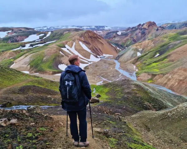 Un randonneur admire le paysage coloré de Landmannalaugar, avec ses montagnes aux teintes ocre, vertes et blanches.