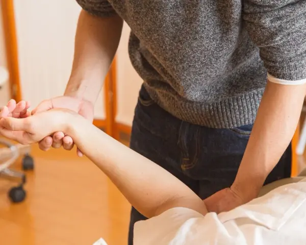 Fizjoterapeuta delikatnie masuje nadgarstek pacjenta, co jest kluczowe, kiedy zacząć rehabilitacja po operacji cieśni nadgarstka.