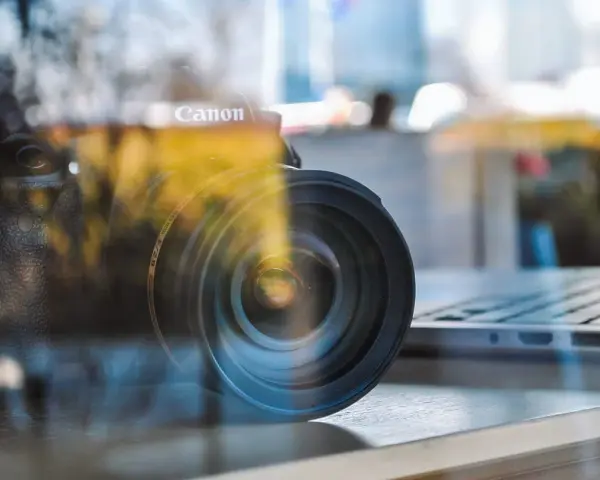 Winieta fotografia: obiektyw Canon na tle laptopa, odbicia tworzą artystyczny efekt.