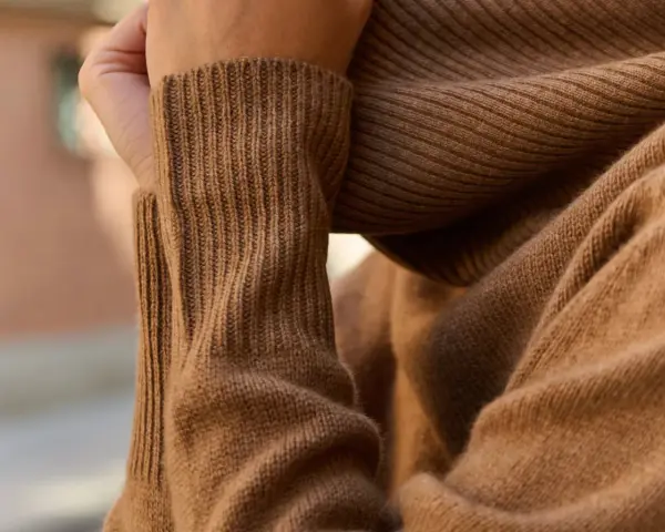 Mano acariciando un suave tejido de kashmir color camel.