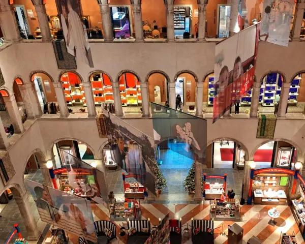 Interno del Fondaco dei Tedeschi, con archi, negozi e grandi stampe appese.