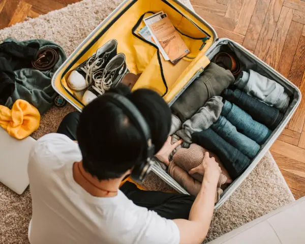 Preparazione per il mare: una valigia piena di vestiti piegati, scarpe, una felpa gialla e un laptop. Ecco cosa portare in vacanza al mare!