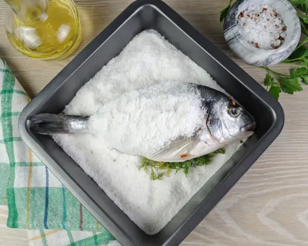 Dorada a la sal lista para hornear, con hierbas frescas y aceite de oliva al lado.