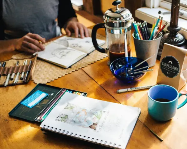 Kreative Inspiration am **cafe impuls**: Skizzenbuch, Stifte, Kaffee und eine Tasse laden zum Malen ein.