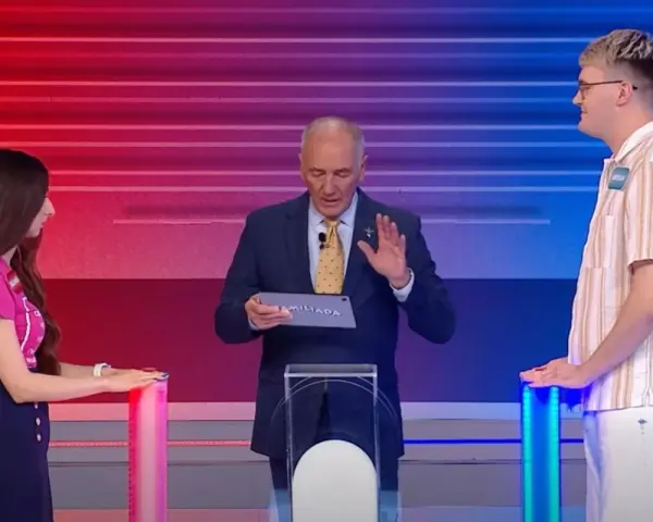 Na planie Familiady, prowadzący trzyma tablet z napisem "FAMILIADA". Po bokach stoją uczestnicy.