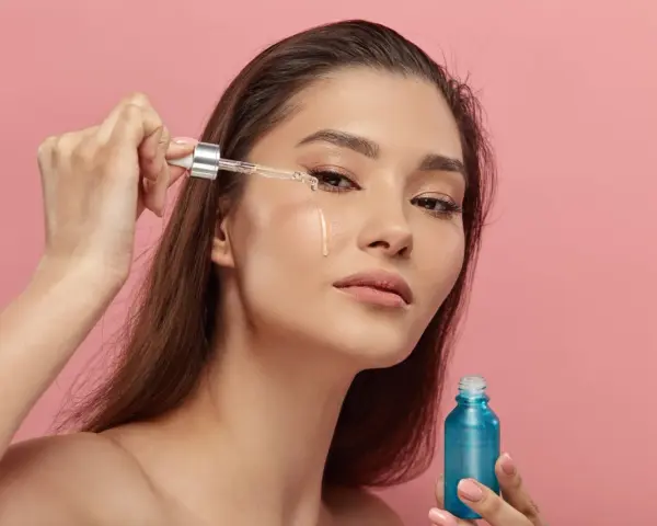 Kobieta aplikuje serum z retinyl palmitate na skórę pod okiem. Błękitna buteleczka kosmetyku w dłoni.