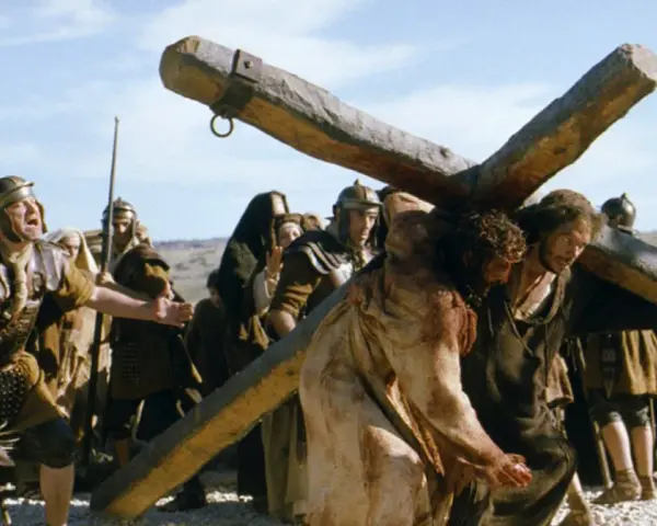 Scena z filmów chrześcijańskich: Jezus dźwigający krzyż, otoczony przez żołnierzy.