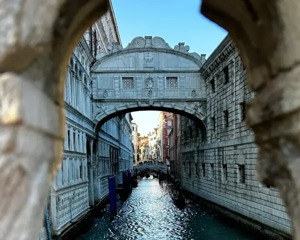 Il Ponte dei Sospiri a Venezia, visto da un'arcata, con gondole sull'acqua e un cielo azzurro.