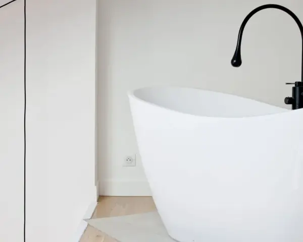 Baignoire îlot blanche au design moderne, avec robinetterie noire. Sa forme suggère une largeur baignoire standard, idéale pour un confort optimal.