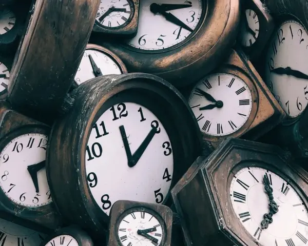 Stos starych zegarów, niektóre z rzymskimi cyframi, inne z arabskimi.