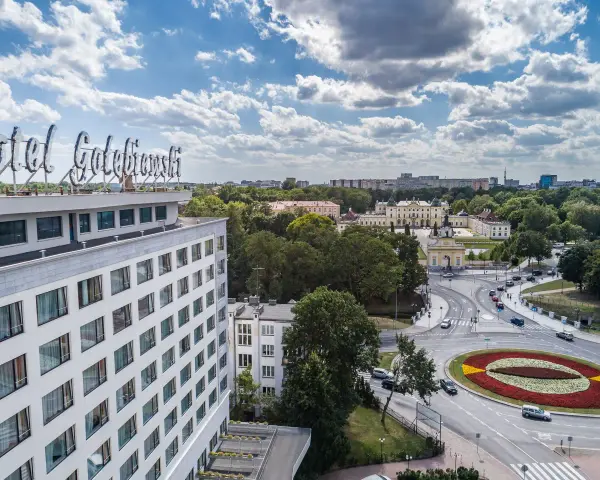 Widok na hotel Gołębiewski w Łodzi z charakterystycznym neonem. W tle rozciąga się miasto z zielenią i budynkami.