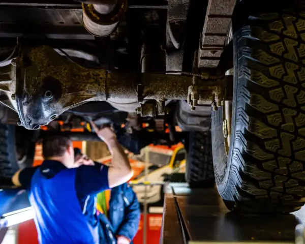 Mechanik sprawdza podwozie terenowego auta z napędem **awd**. Widoczna jest masywna oś i bieżnik opony.