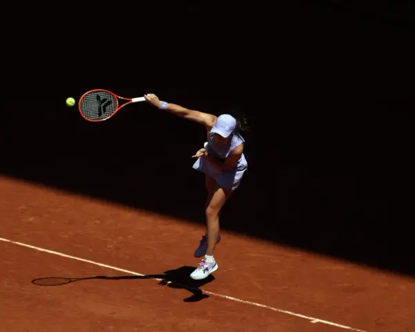 Tenisistka w skoku serwuje piłkę na korcie ziemnym podczas Roland Garros.