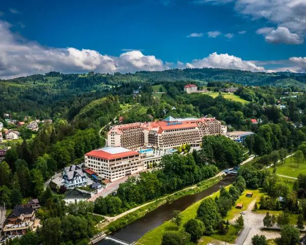Hotel Gołębiewski w otoczeniu zielonych wzgórz i rzeki.