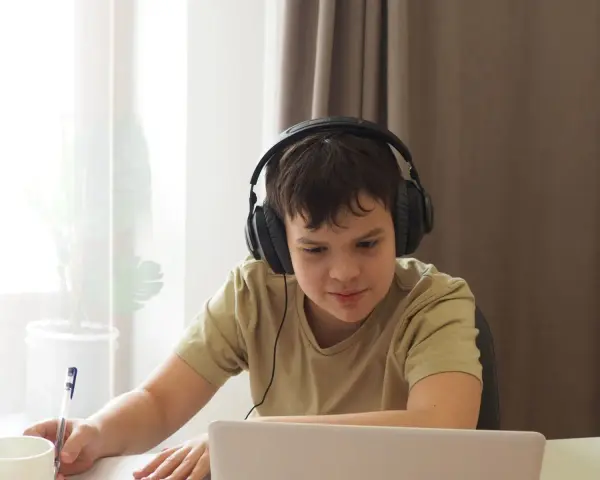 Chłopiec w słuchawkach uczy się zdalnie, notując. Dopełnienie odpowiada na pytania: kogo? czego? komu? czemu? kogo? co? czym? kim? o kim? o czym?